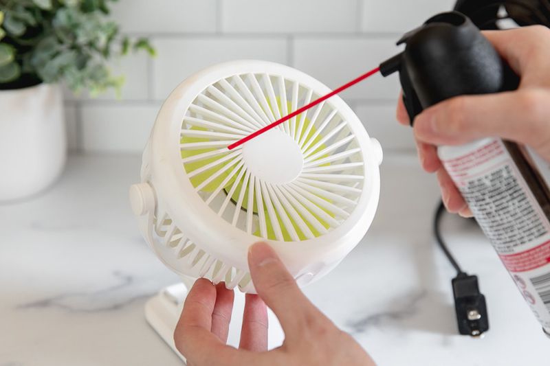 A collection of cleaning tools including a microfiber cloth, vacuum attachment, and mild soap laid out next to a fan