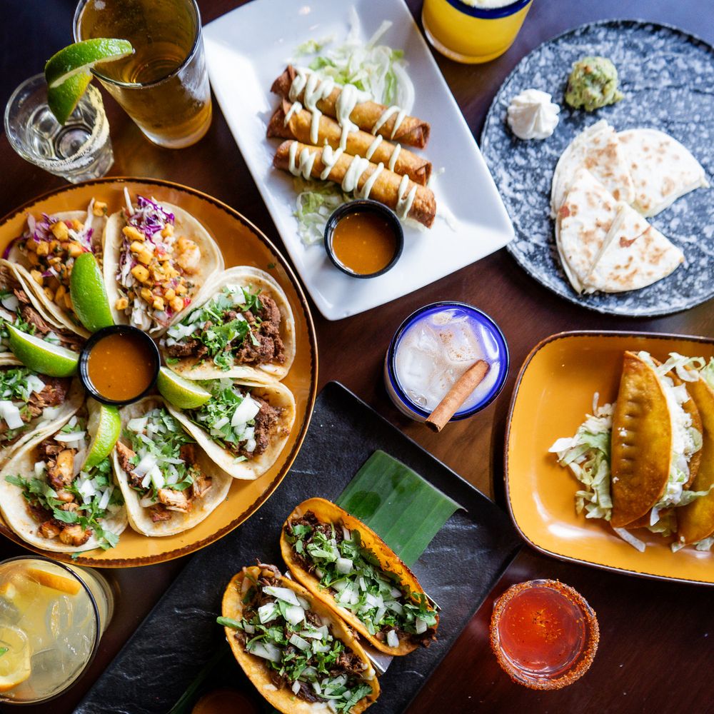 A vibrant spread of authentic Mexican tacos, fresh guacamole, and lime wedges on a wooden table