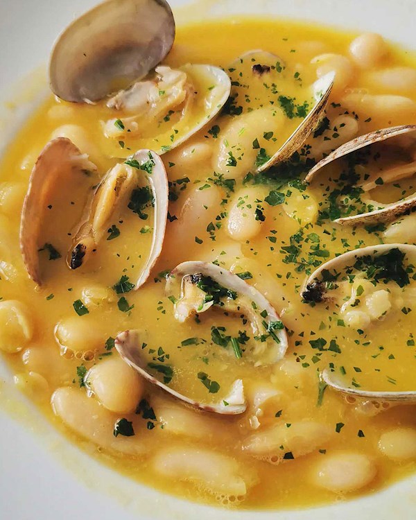 Close up of Fabes con Almejas showing the light green parsley and saffron broth