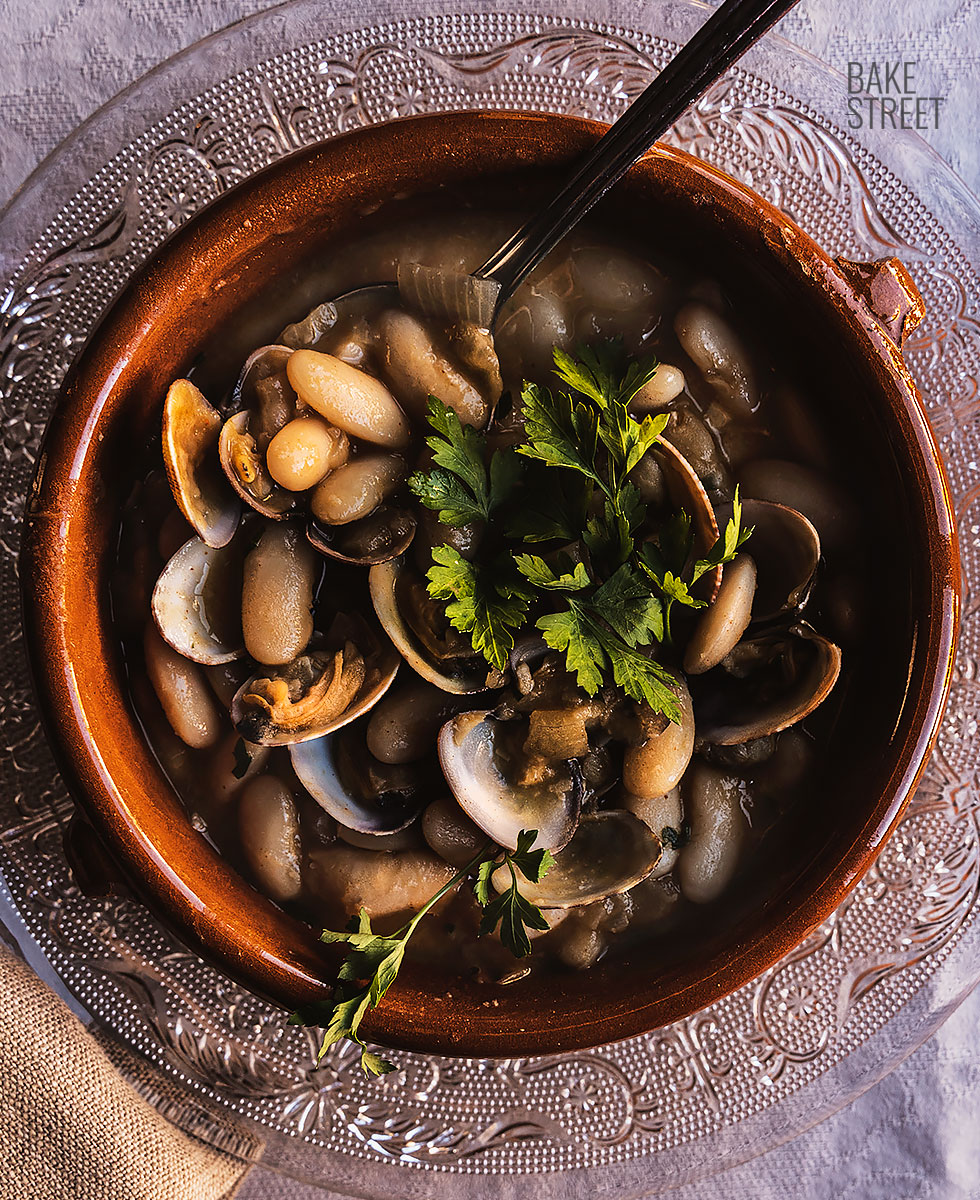 Chef preparing fabes con almejas in a traditional wide pan