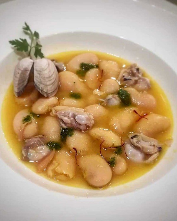 A rustic presentation of Spanish beans and clams in a terracotta bowl